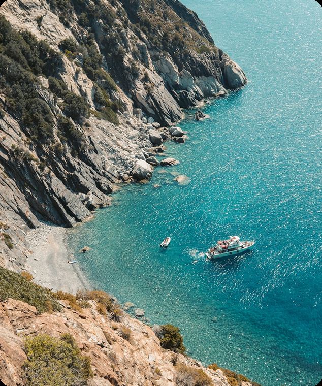 Rocky cliff dropping into turquoise water with a boat at anchor