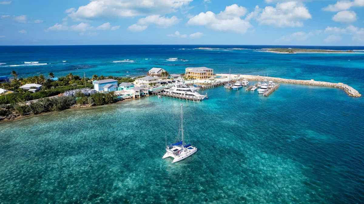 Catamaran anchored in turquoise waters off a tropical island with a marina