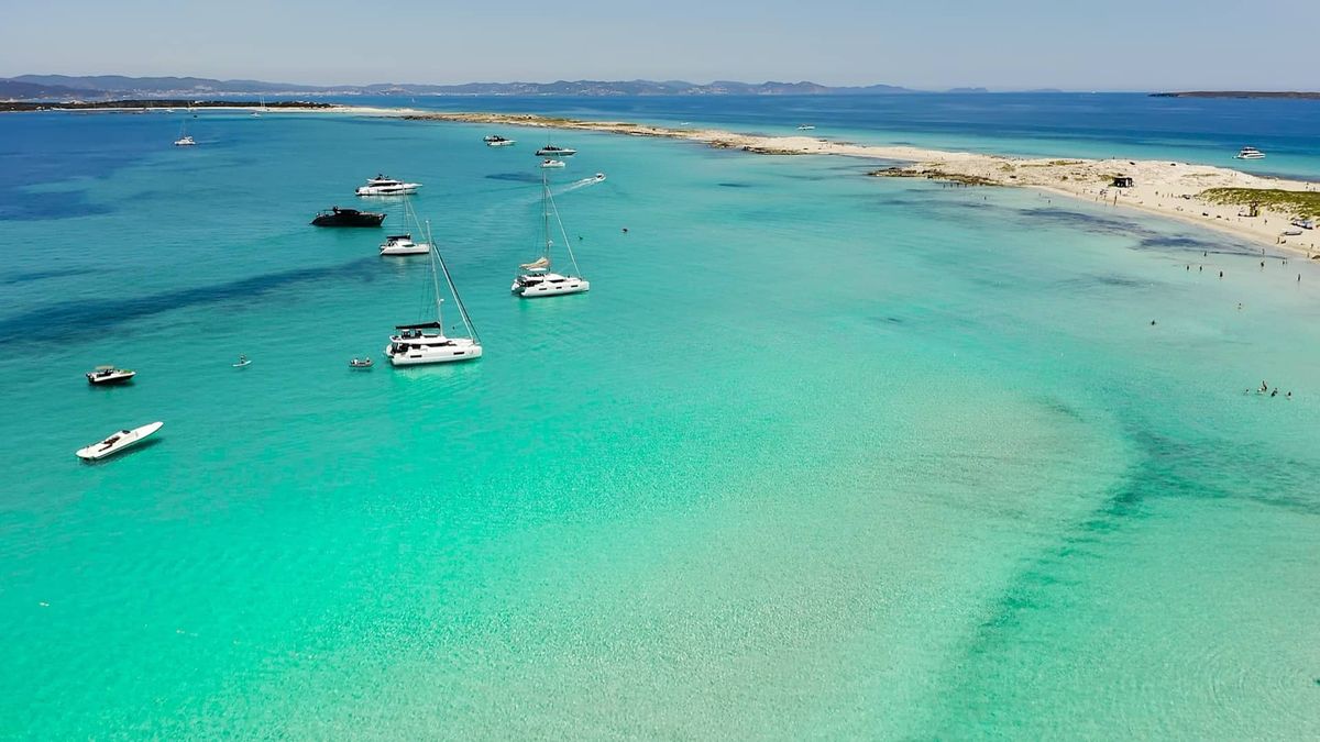 Catamarans anchored in turquoise waters off a white beach in the Balearic Islands